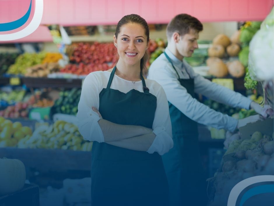 BlogSGSistemas23 Funcionária em mercado com frutas e verduras ao fundo.